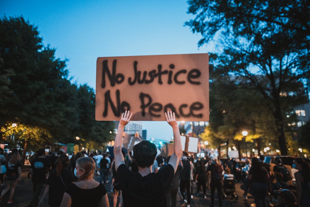 A diverse crowd gathers peacefully, holding signs demanding justice in an evening protest.